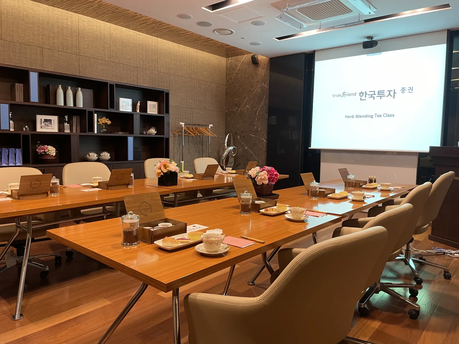 티클래스 인원 프로젝터 스크린과 책장이 있는 회의실에 블렌딩 클래스 테이블이 세팅된 전경