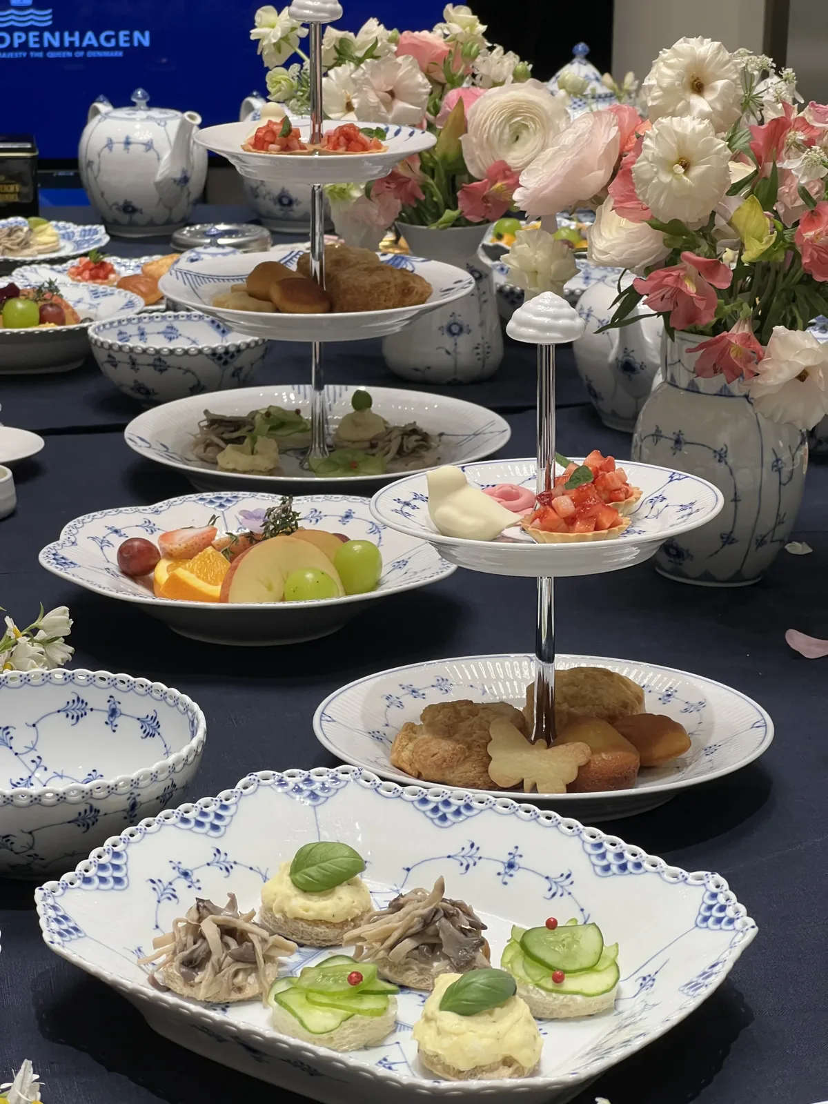 티클래스 꽃장식 연분홍과 흰 꽃이 꽂힌 화병 옆에 3단 스탠드와 접시에 담긴 다과가 놓인 테이블