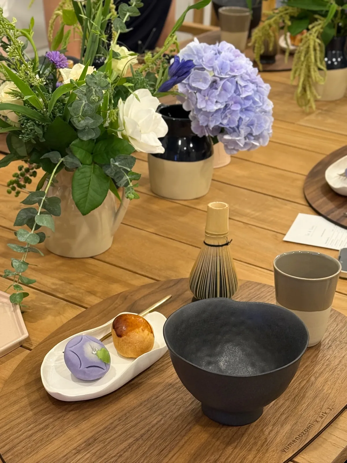 생일 티클래스 보라색 수국과 꽃 장식 옆에 말차 솔과 화과자, 검은 그릇이 놓인 테이블